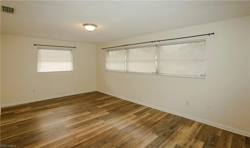 Spacious room featuring wood-finish flooring, light-colored walls, and multiple windows with blinds