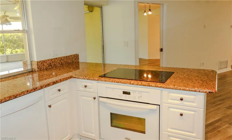 Kitchen featuring white cabinetry, polished granite countertops with a matching backsplash, a built-in oven, and a ceramic cooktop