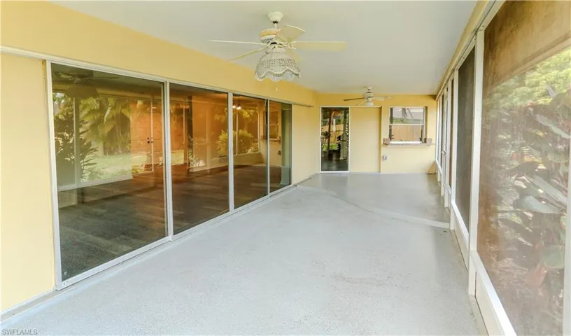 Expansive screened patio featuring a textured concrete floor, multiple ceiling fans, and a long wall of sliding glass doors