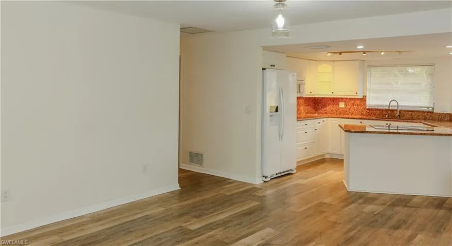 Kitchen featuring white cabinetry, granite countertops, a built-in sink, and a contrasting red-toned backsplash