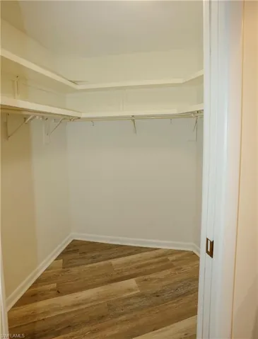 Walk-in closet featuring wood-finish flooring, white baseboards, and built-in shelving with hanging rods
