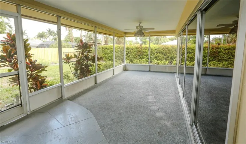 Spacious screened patio featuring textured concrete flooring, dual ceiling fans, and a partial view of the surrounding landscape
