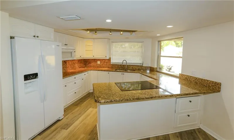 Kitchen featuring white cabinetry, granite-finish countertops, tile backsplash, wood-finish flooring, and recessed lighting