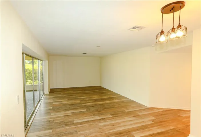 Spacious room featuring wood-finish flooring, light-colored walls, and a contemporary three-light pendant fixture