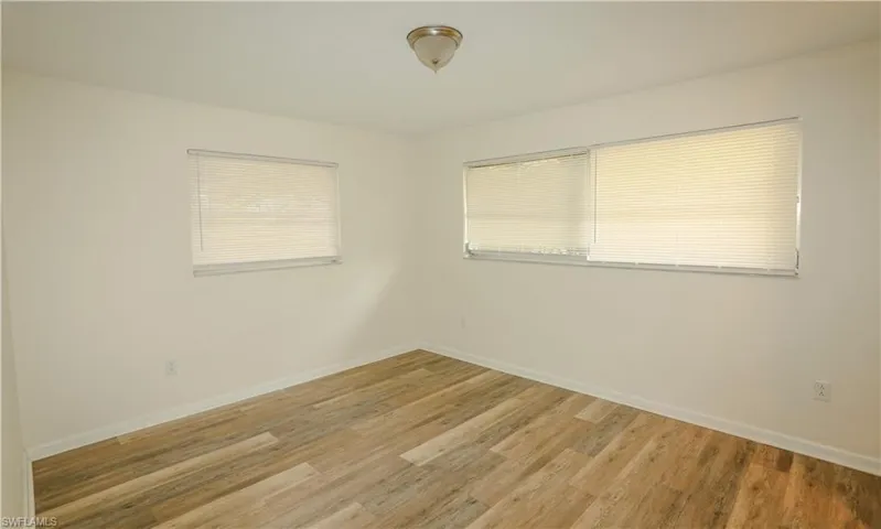 Interior room featuring wood-finish flooring, two windows with blinds, a neutral wall color, and a ceiling-mounted light fixture