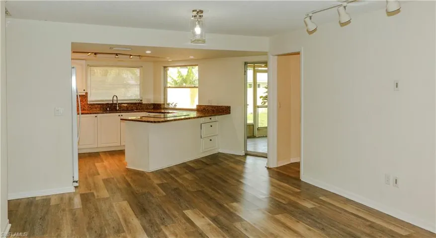 Open-concept interior featuring wood-finish flooring, white walls, and a recessed kitchen area