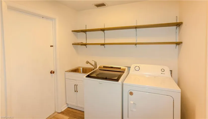 Dedicated utility space featuring a stainless steel sink, white base cabinetry with brushed nickel pulls, and wood-finish open shelving