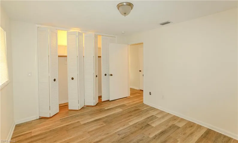 Bedroom featuring wood-finish flooring, white walls, and louvered bifold closet doors