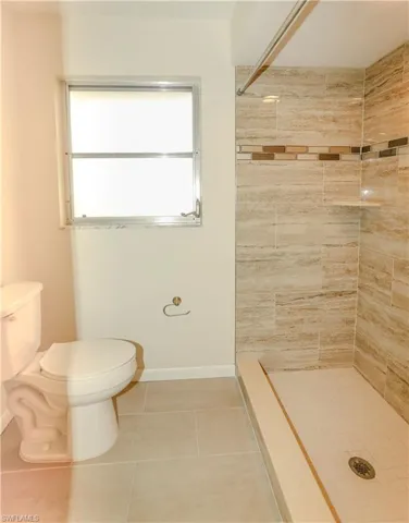Shower stall featuring large-format stone-look tile, a decorative accent band, and a built-in corner shelf