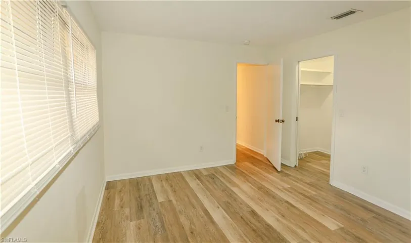 Room featuring wood-finish flooring, white baseboards, and a window with horizontal blinds