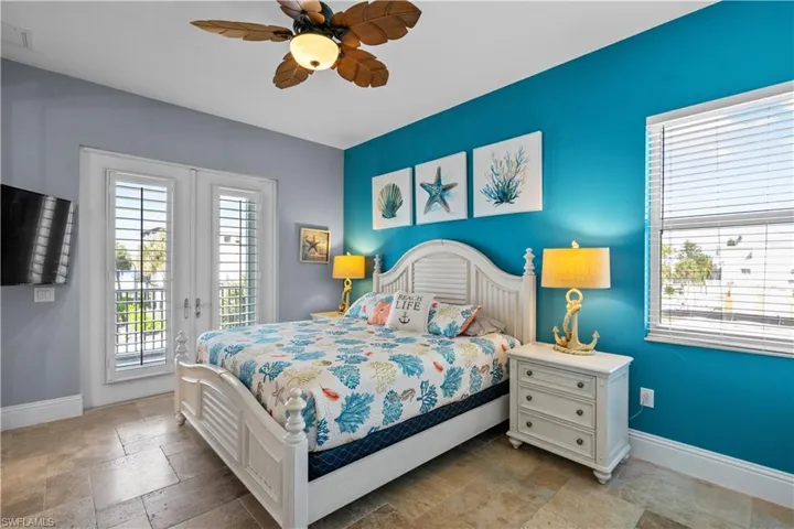 Bedroom featuring a vibrant accent wall, tile flooring, a ceiling fan, and French doors with plantation shutters