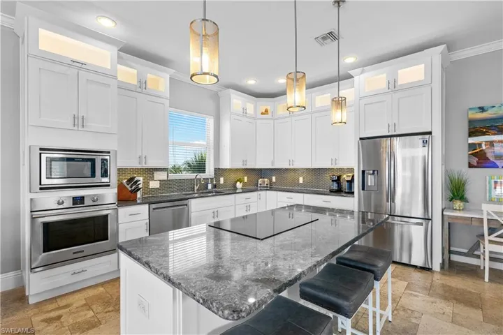 Spacious kitchen featuring white cabinetry, a large center island with a cooktop, stainless steel appliances, and a tiled backsplash
