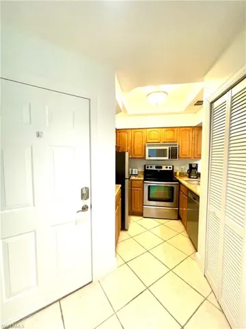 Kitchen featuring appliances with stainless steel finishes, light countertops, light tile patterned flooring, brown cabinetry, and a tray ceiling