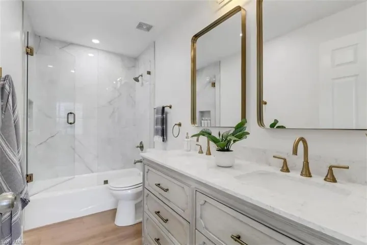 Full bathroom with vanity, toilet, wood-type flooring, and enclosed tub / shower combo