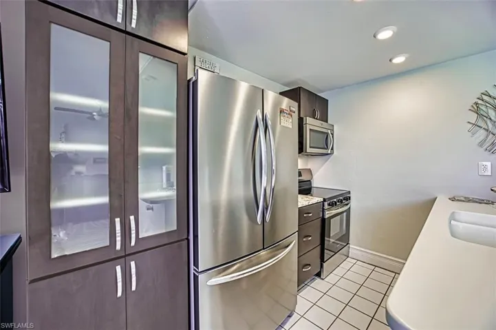 Kitchen with appliances with stainless steel finishes, dark brown cabinets, light tile patterned floors, glass insert cabinets, and recessed lighting