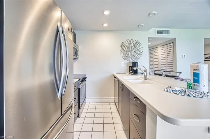 Kitchen featuring appliances with stainless steel finishes, light tile patterned floors, recessed lighting, a breakfast bar, and dark brown cabinets