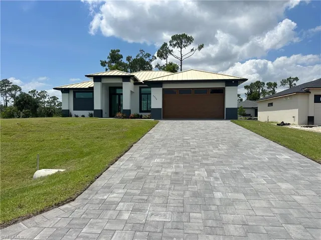 Prairie-style house featuring stucco siding, a standing seam roof, decorative driveway, a garage, and a front lawn