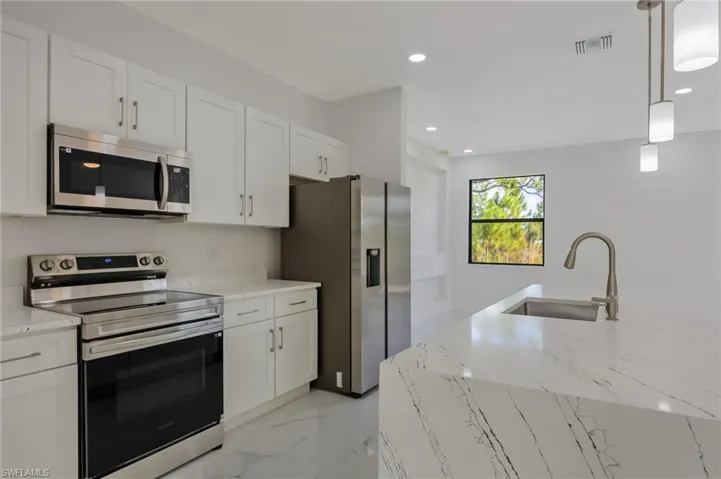 Kitchen with stainless steel appliances, light stone counters, hanging light fixtures, white cabinetry, and light marble finish floors
