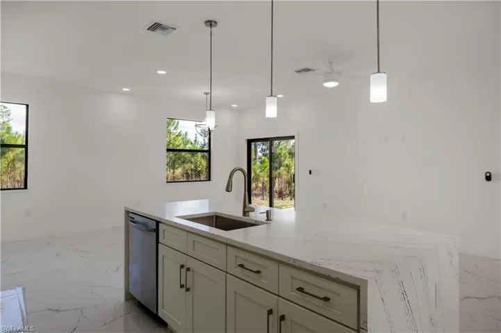 Kitchen featuring light marble finish flooring, a center island with sink, light stone counters, and decorative light fixtures