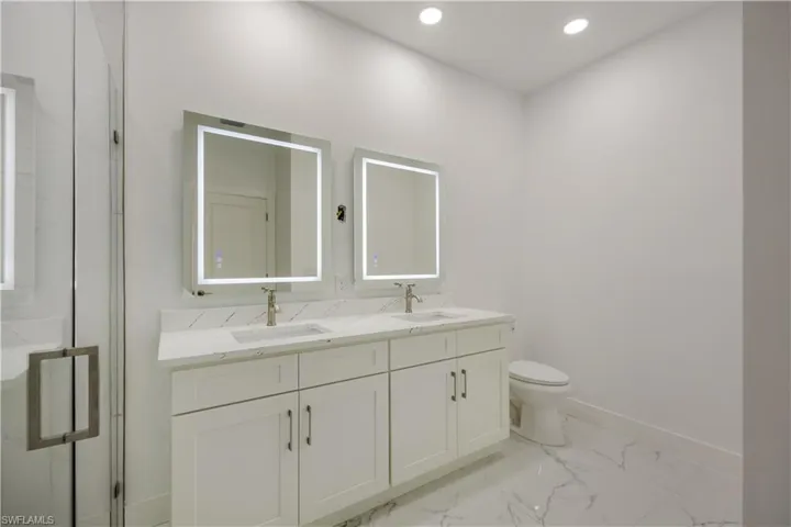 Full bathroom featuring double vanity, a marble finish shower, recessed lighting, and light marble finish floors