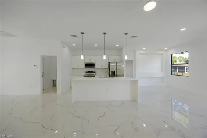 Kitchen featuring open floor plan, an island with sink, hanging light fixtures, stainless steel appliances, and white cabinets