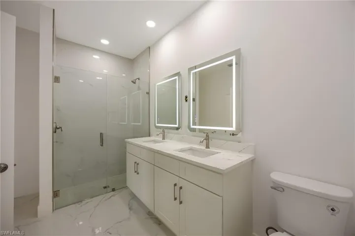 Bathroom with a marble finish shower, double vanity, light marble finish flooring, and recessed lighting