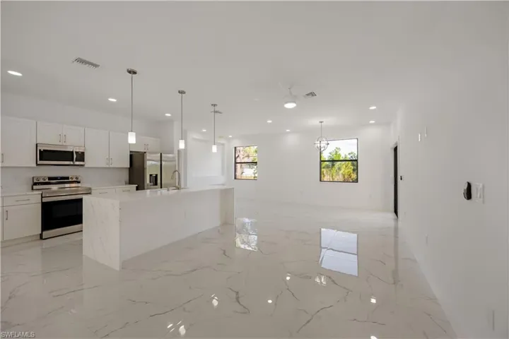 Kitchen featuring stainless steel appliances, an island with sink, open floor plan, pendant lighting, and white cabinetry