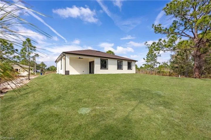 Back of house featuring stucco siding, a ceiling fan, and a lawn