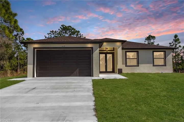 Prairie-style home featuring a front lawn, concrete driveway, stucco siding, roof with shingles, and an attached garage