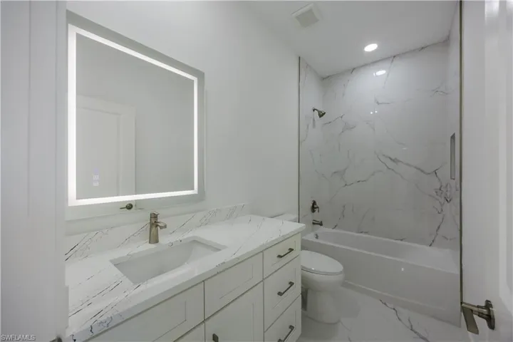 Bathroom featuring vanity, tub / shower combination, light marble finish flooring, and recessed lighting