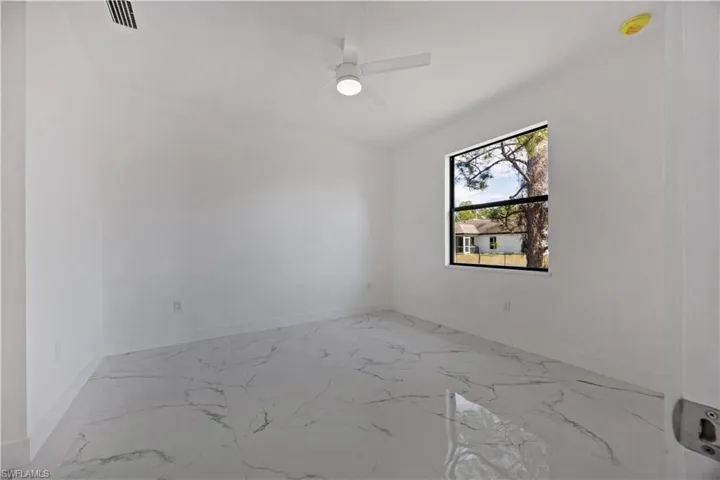 Empty room featuring light marble finish flooring and a ceiling fan