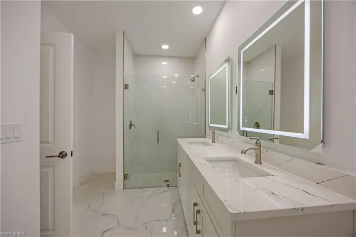 Bathroom with a marble finish shower, double vanity, recessed lighting, and light marble finish flooring