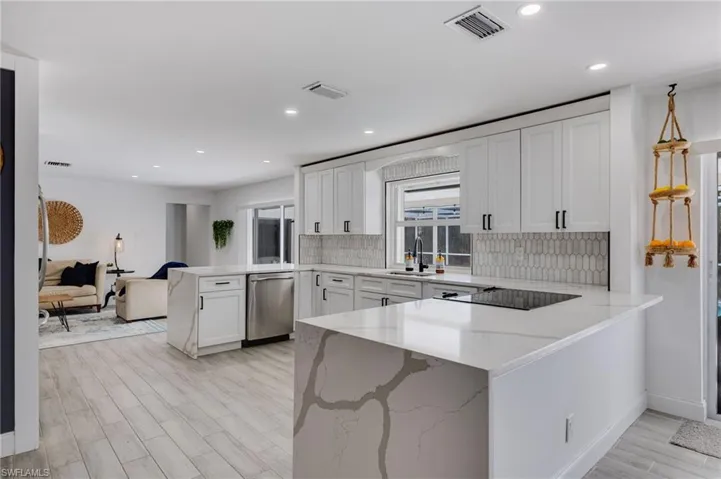 Kitchen featuring a peninsula, light stone counters, white cabinetry, open floor plan, and stainless steel dishwasher