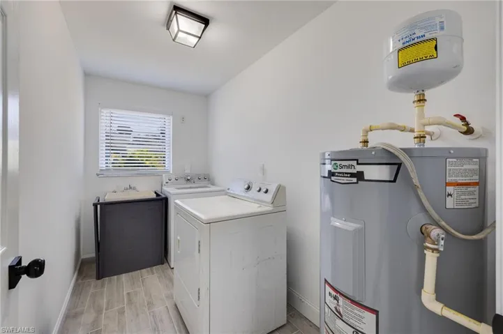 Laundry room with electric water heater, washing machine and clothes dryer, and wood tiled floors
