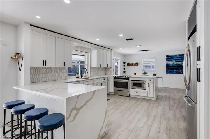 Kitchen featuring a peninsula, white cabinets, light stone counters, a breakfast bar area, and recessed lighting