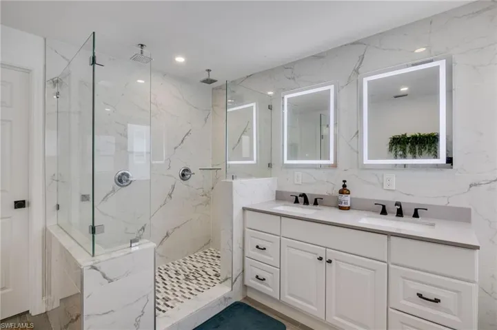 Bathroom with double vanity, a marble finish shower, stone wall, recessed lighting, and tile walls