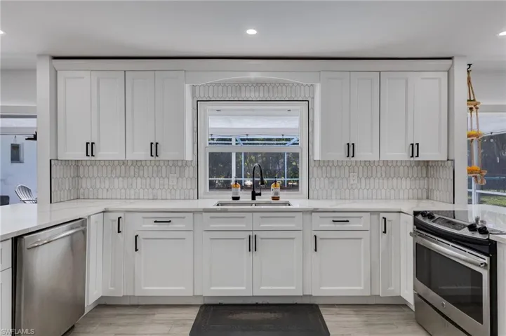 Kitchen with stainless steel appliances, white cabinetry, light stone counters, a peninsula, and recessed lighting