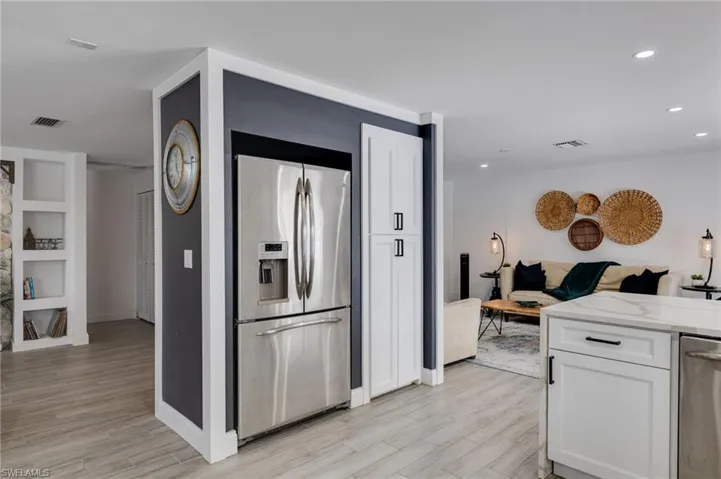 Kitchen with open floor plan, stainless steel appliances, white cabinetry, light stone counters, and wood finish floors