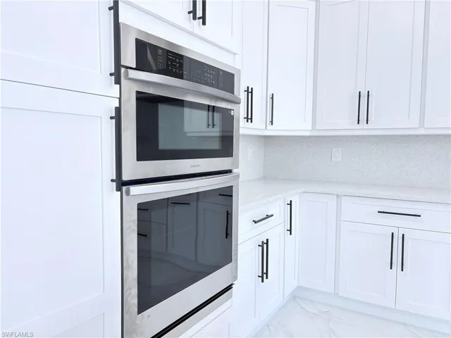 Kitchen featuring light stone counters, white cabinets, double oven, and decorative backsplash