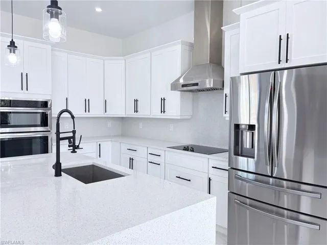 Kitchen with wall chimney exhaust hood, sink, stainless steel appliances, light stone countertops, and white cabinets