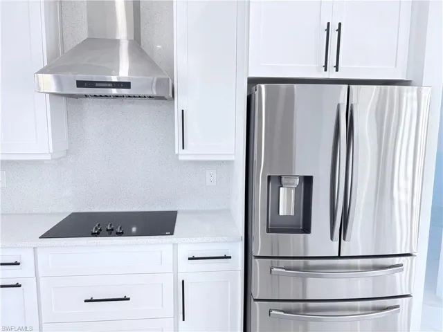 Kitchen featuring white cabinetry, wall chimney exhaust hood, stainless steel fridge, and backsplash