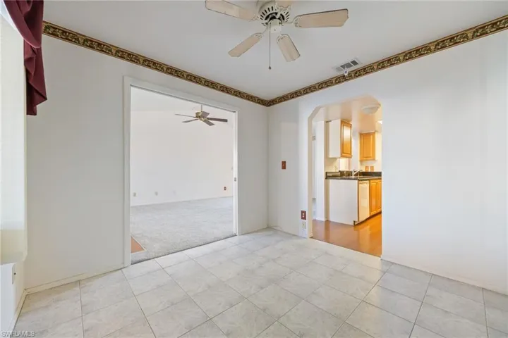 Unfurnished room featuring a ceiling fan, light colored carpet, arched walkways, and light tile patterned floors