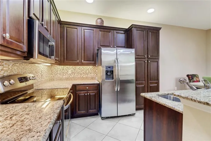 Kitchen featuring stainless steel appliances, light stone counters, dark wood finish cabinetry, and recessed lighting