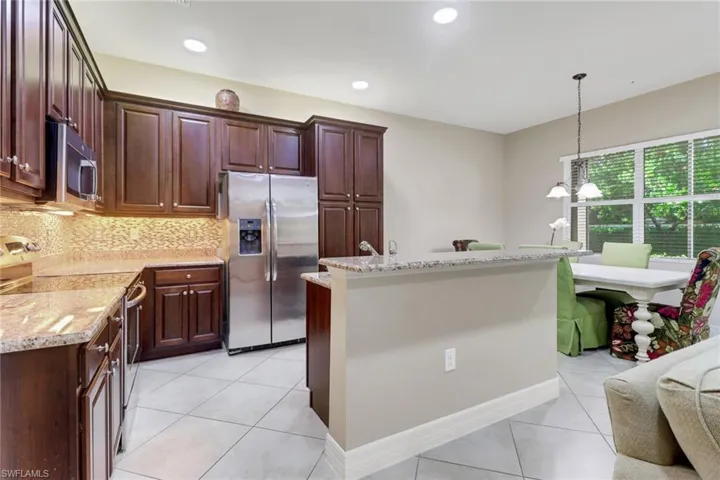 Kitchen featuring stainless steel appliances, a kitchen island with sink, light tile patterned floors, light stone counters, and backsplash