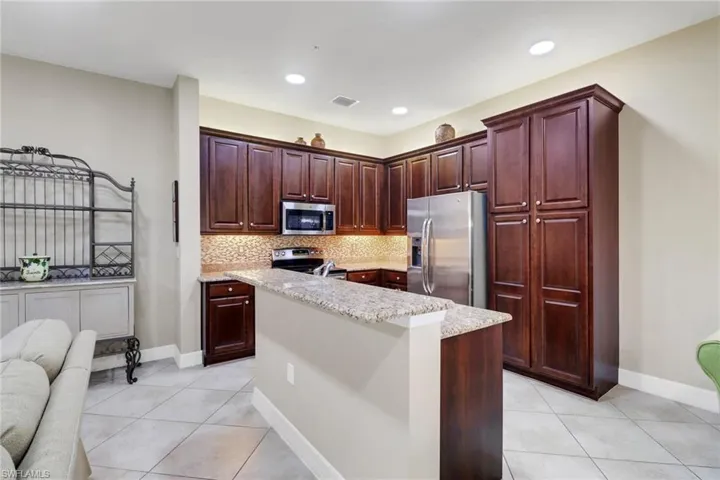 Kitchen with stainless steel appliances, light tile patterned floors, a kitchen island with sink, and backsplash