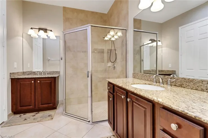 Bathroom featuring two vanities, a shower stall, and light tile patterned floors