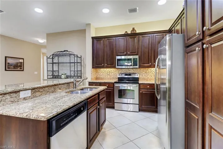 Kitchen featuring stainless steel appliances, light stone countertops, dark wood finish cabinets, a kitchen island with sink, and light tile patterned flooring