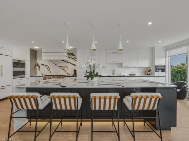 Kitchen with light wood finished floors, a spacious island, light stone counters, a breakfast bar area, and decorative light fixtures