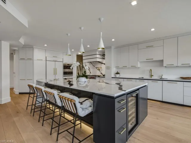 Two tone kitchen featuring a breakfast bar area, light wood finished floors, two tone cabinets, decorative light fixtures, and beverage cooler