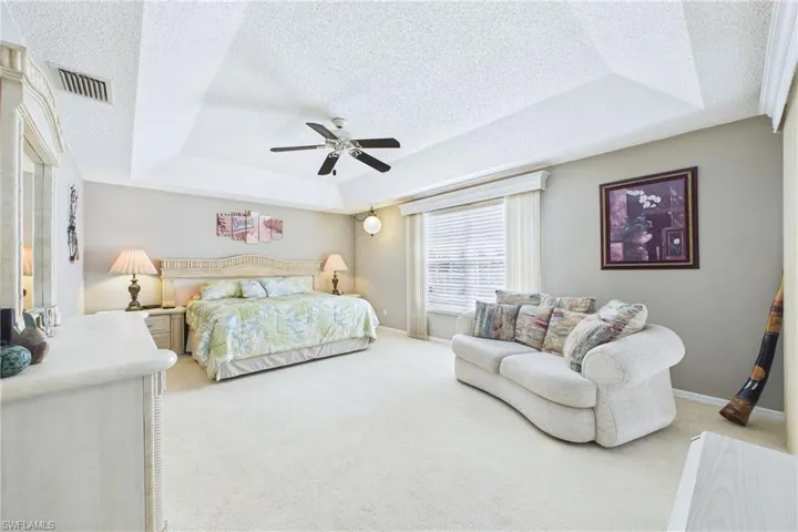 LARGE Primary Bedroom with a textured ceiling, a ceiling fan, light colored carpet, and a raised ceiling
